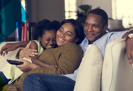 Photograph of a family of people of colour on a sofa cuddling and looking happy