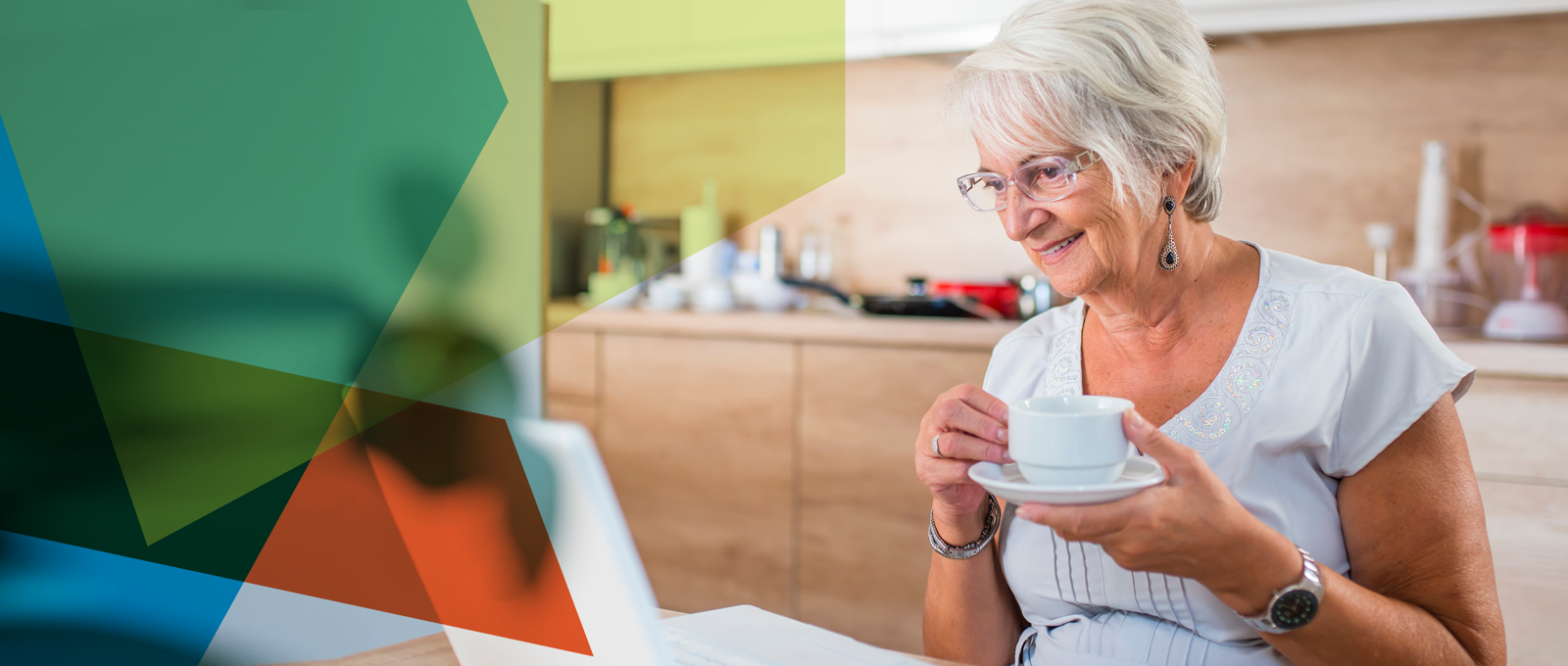 Photograph of an older woman holding a teacup in her kitchen and looking at a laptop