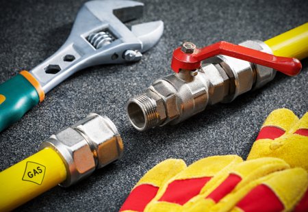 Close-up photograph of a disconnected gas pipe, a safety glove and a spanner