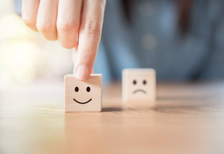 Photograph of two wooden blocks on a table. One has a smiley face on it, the other a sad face. Someone's hand is pushing the smiley one to the front.